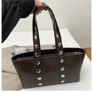 Close-up of a dark brown tote bag with large silver rivets and a metal zipper closure
