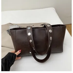 Detailed view of dark brown leather tote with silver stud accents on wide shoulder strap