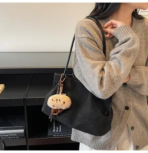 Detail of black suede shoulder bag with a cute plush charm in a minimalist interior