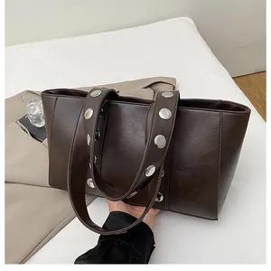 Detail of dark coffee tote bag featuring silver rivets on handles and premium faux leather