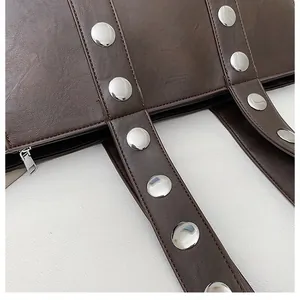 Macro detail of dark brown leather tote with silver rivets and metal zipper closure