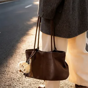 Brown faux suede tote bag with plush charm and tassel pendant shown in outdoor setting