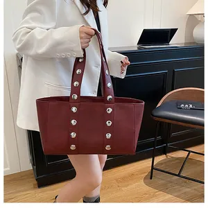 Detail of dark red tote bag with silver studs on leather strap in office setting