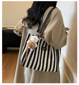 Detail of striped canvas tote with black leather straps and cute plush bear accessory