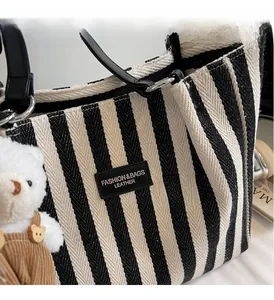 Detailed close-up of striped canvas tote bag with leather logo patch and cute bear charm
