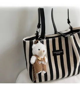 Detail of striped canvas tote bag with black leather label and teddy bear charm
