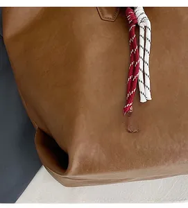 Dettaglio di una borsa tote in pelle marrone con eleganti ciondoli in corda intrecciata