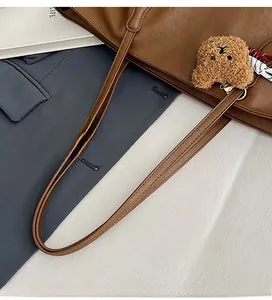 Dettaglio di una borsa tote in pelle marrone con ciondolo a forma di orsetto e nastro