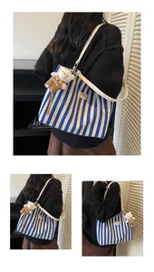 Detail of blue striped canvas tote with brand label, leather straps and a plush bear charm