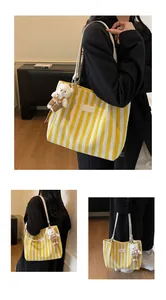 Macro view of a striped canvas tote bag featuring a plush bear charm and leather logo