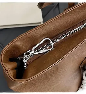 Dettaglio della cerniera argentata e degli accessori su borsa tote in pelle marrone
