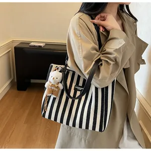 Striped canvas tote bag with black leather straps and plush bear charm on model