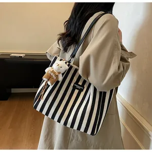 Detail of striped canvas tote bag with black straps and a cute plush bear charm