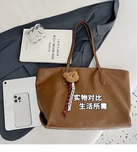 Vista piatta della grande borsa tote marrone con ciondolo a orsetto, tablet e libri