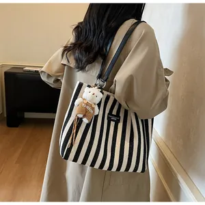 Detail showing striped canvas tote bag with black leather straps and a plush bear charm