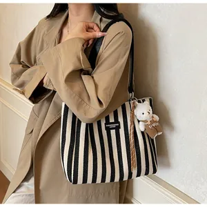 Striped canvas tote bag detail showing the leather logo tag and plush bear accessory