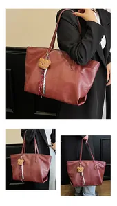 Dettaglio della borsa tote bordeaux con ciondolo a forma di orsetto e nappa a righe sul manico