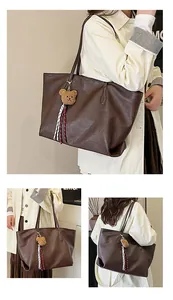 Dettaglio della borsa tote marrone vintage con ciondolo a forma di orsetto e nastro a righe