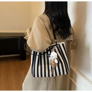 Detail of striped canvas tote with leather straps and a cute teddy bear charm accessory