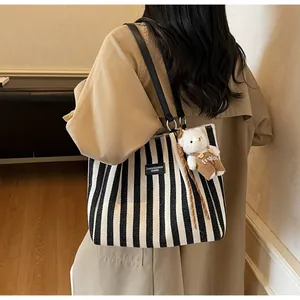 Detail of striped canvas tote bag with a small plush bear charm and black leather tag