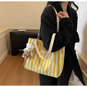 Detailed view of yellow striped canvas tote bag featuring a cute plush bear pendant