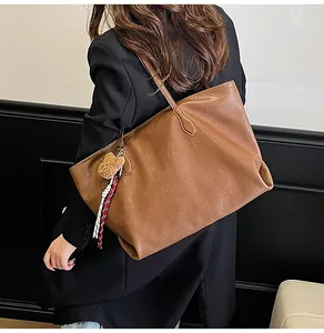 Dettaglio di una borsa tote in pelle marrone con ciondolo a orsetto e foulard