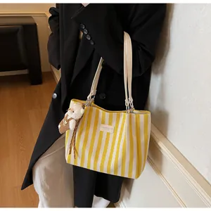 Detail of yellow striped canvas tote with soft bear charm and leather shoulder straps