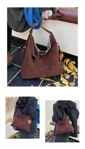 Detail of a brown suede hobo bag featuring a floral charm and heart-shaped zipper pull