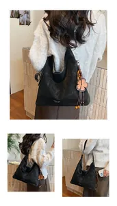 Detail of black suede tote bag with floral pendant and tassel charm in warm light