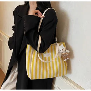 Detail of yellow striped canvas tote bag with a small plush bear charm on the strap