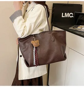 Dettaglio di una borsa tote marrone capiente con ciondolo a forma di orso su una modella