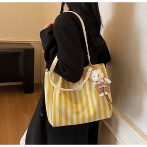 Detailed shot of yellow and white striped canvas tote with leather strap and plush bear charm