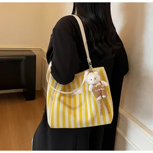 Detail of yellow striped canvas tote bag with a cute plush bear charm on a slim strap