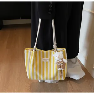 Detail of yellow striped canvas tote with leather strap and plush bear charm
