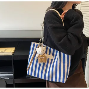 Detail of blue striped canvas tote bag featuring a cute teddy bear charm on shoulder