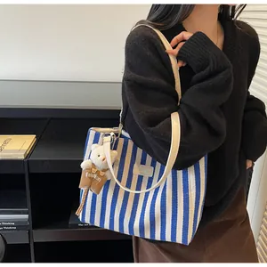Detail of blue and white striped canvas tote bag with a small plush bear charm attached
