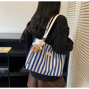 Close-up of blue striped canvas tote bag with white leather straps and plush bear charm