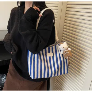 Detail shot of a blue and white striped canvas tote bag featuring a cute teddy bear charm