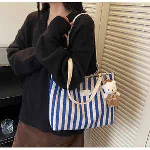Detail of blue and white striped canvas tote bag featuring a cute plush bear pendant accessory