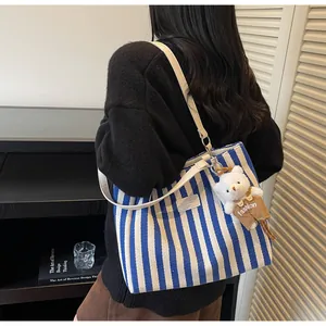 Close-up of blue striped canvas tote bag with leather straps and a cute plush bear charm