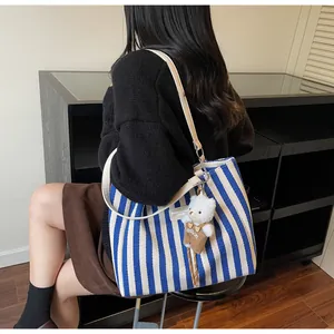 Detail of blue striped canvas tote bag featuring a cute plush bear charm and leather strap