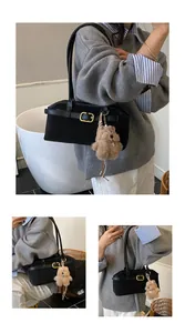Detail of black minimalist shoulder bag with gold clasp and plush bear charm accent