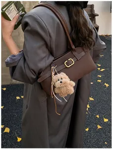 Detail of a dark brown matte leather shoulder bag with gold hardware and plush bear charm