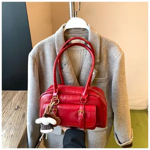 Close-up of vibrant red leather shoulder bag with gold buckles and plush doll charm