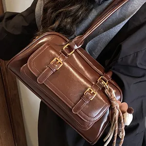 Deep brown glossy underarm bag with vintage design and heart tassel detail on model