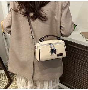 Dettaglio della borsa a scatola crema con finiture marroni e ciondolo robot sulla spalla