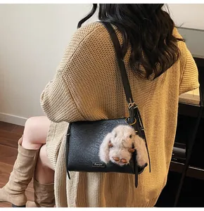 Detail of black shoulder bag featuring a cute brown plush rabbit pendant on the side