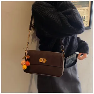 Detail der braunen quadratischen Tasche mit goldenem Drehverschluss und buntem Fruchtanhänger