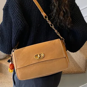 Klassische kamelfarbene Umhängetasche mit Goldschnalle und Kette auf schwarzem Pullover