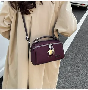 Dettaglio della borsa a scatola bordeaux con cerniera metallica e ciondolo su cappotto beige